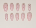 Set of pink nail extensions with embedded rhinestones on a beige background