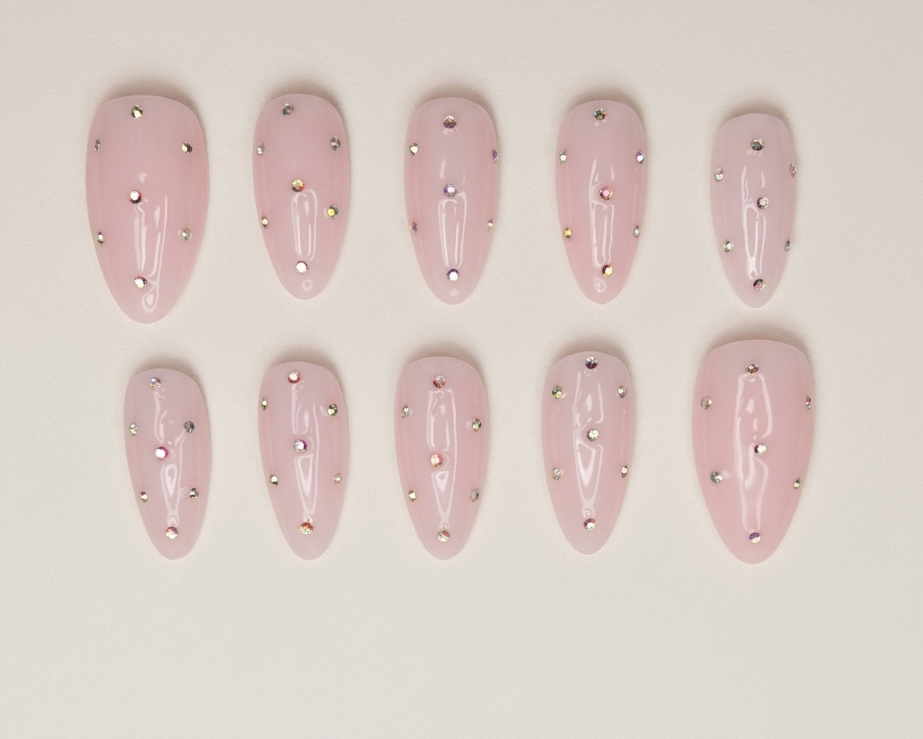 Set of pink nail extensions with embedded rhinestones on a beige background