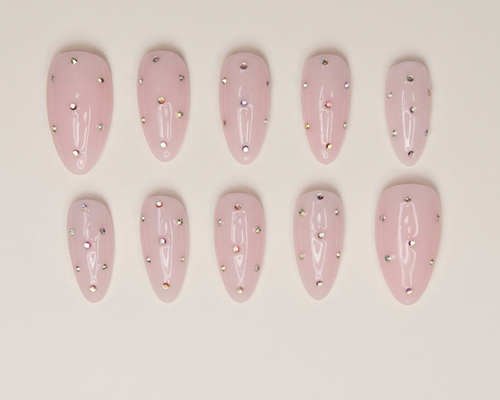 Set of pink nail extensions with embedded rhinestones on a beige background